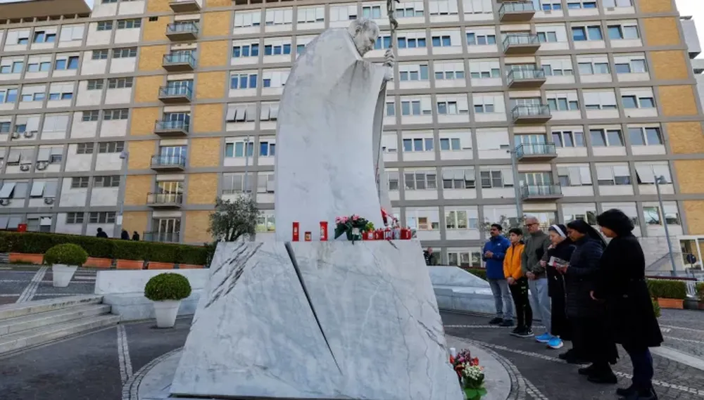 Rezo y esperanza. Varias personas ante la estatua de Juan Pablo II situada frente al hospital Gemelli de Roma, donde está ingresado el Papa. Foto: El País de España