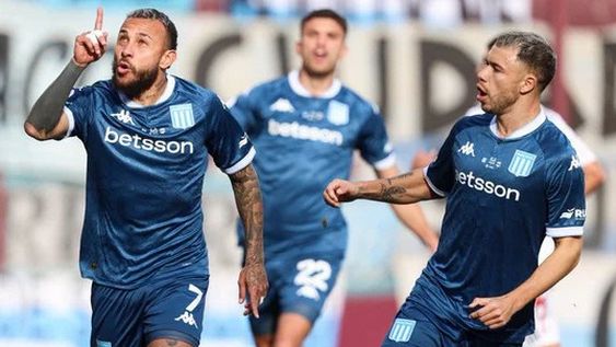 El colombiano Vergara marcó el penal con el que Racing abrió el marcador y lo festeja con sus compañeros. Racing goleó y sigue, en carrera.