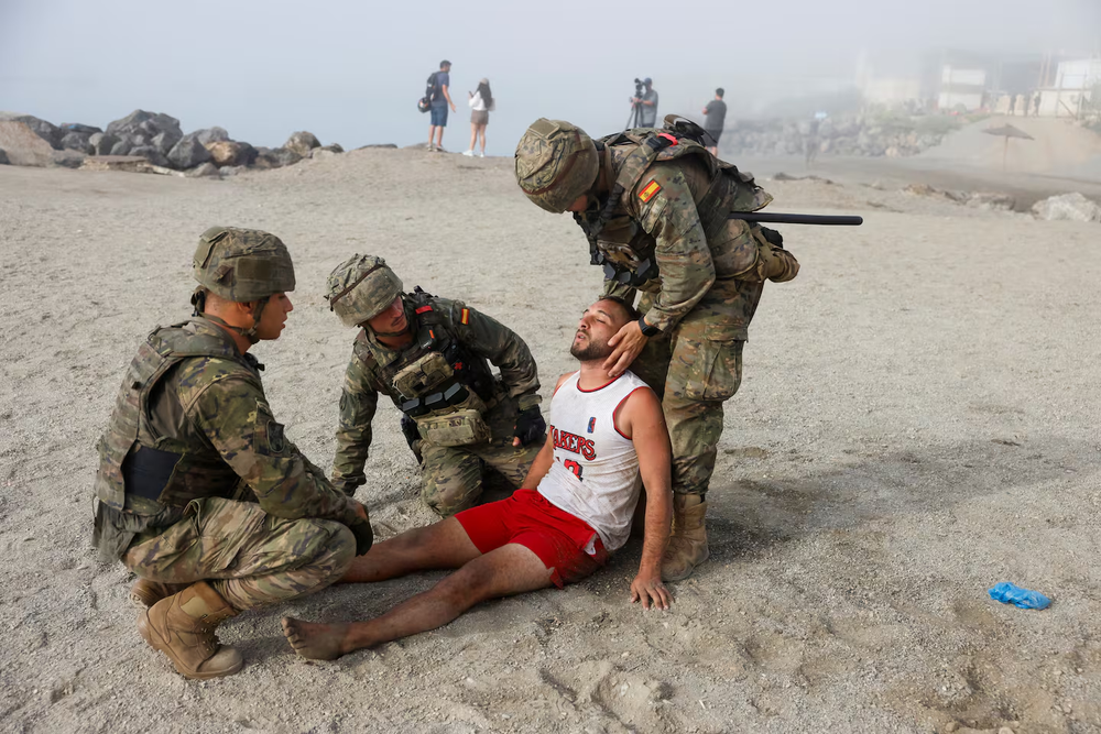 Soldados espa&ntilde;oles asisten a un migrante en una playa de Ceuta. (Foto: REUTERS/Jon Nazca).