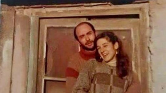 Indio Solari y Virginia sonríen en una tierna imagen de su juventud, abrazándose con cariño frente a una ventana.
